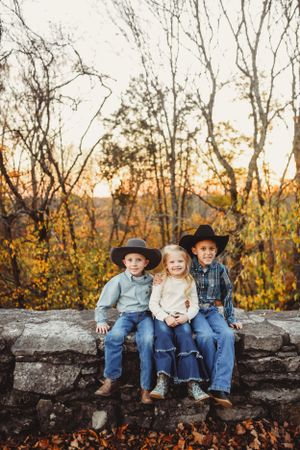 Children sit together on a stone wall with fall trees and golden sunlight in the background.