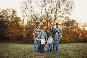 Family portrait session in open field during golden hour with fall foliage.