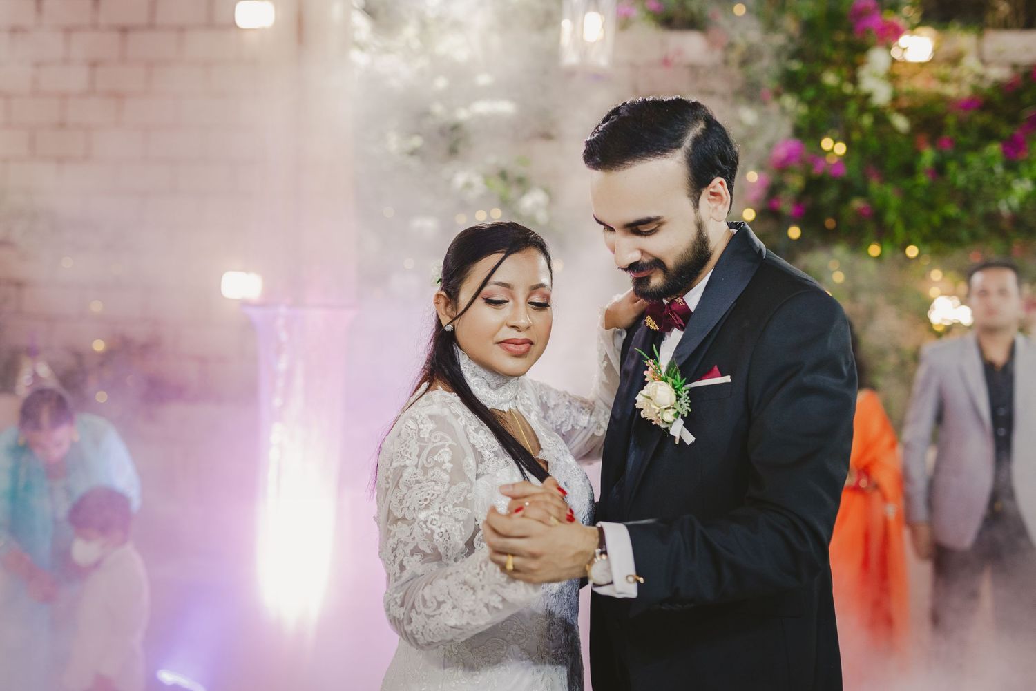 Newlyweds dancing together against a pink-lit backdrop with floral decorations.