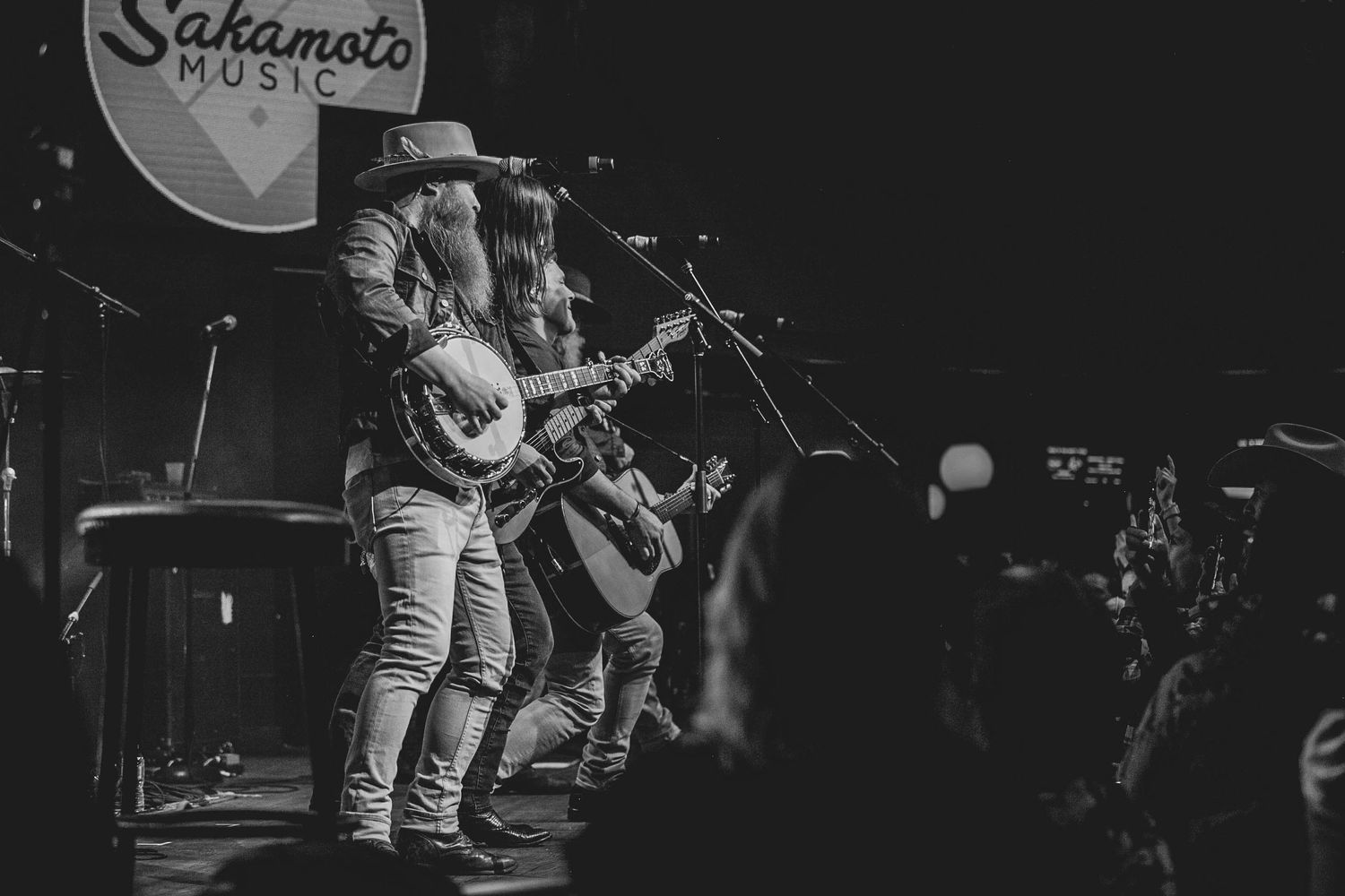 Musicians performing on stage at Sakamoto Music venue in black and white.