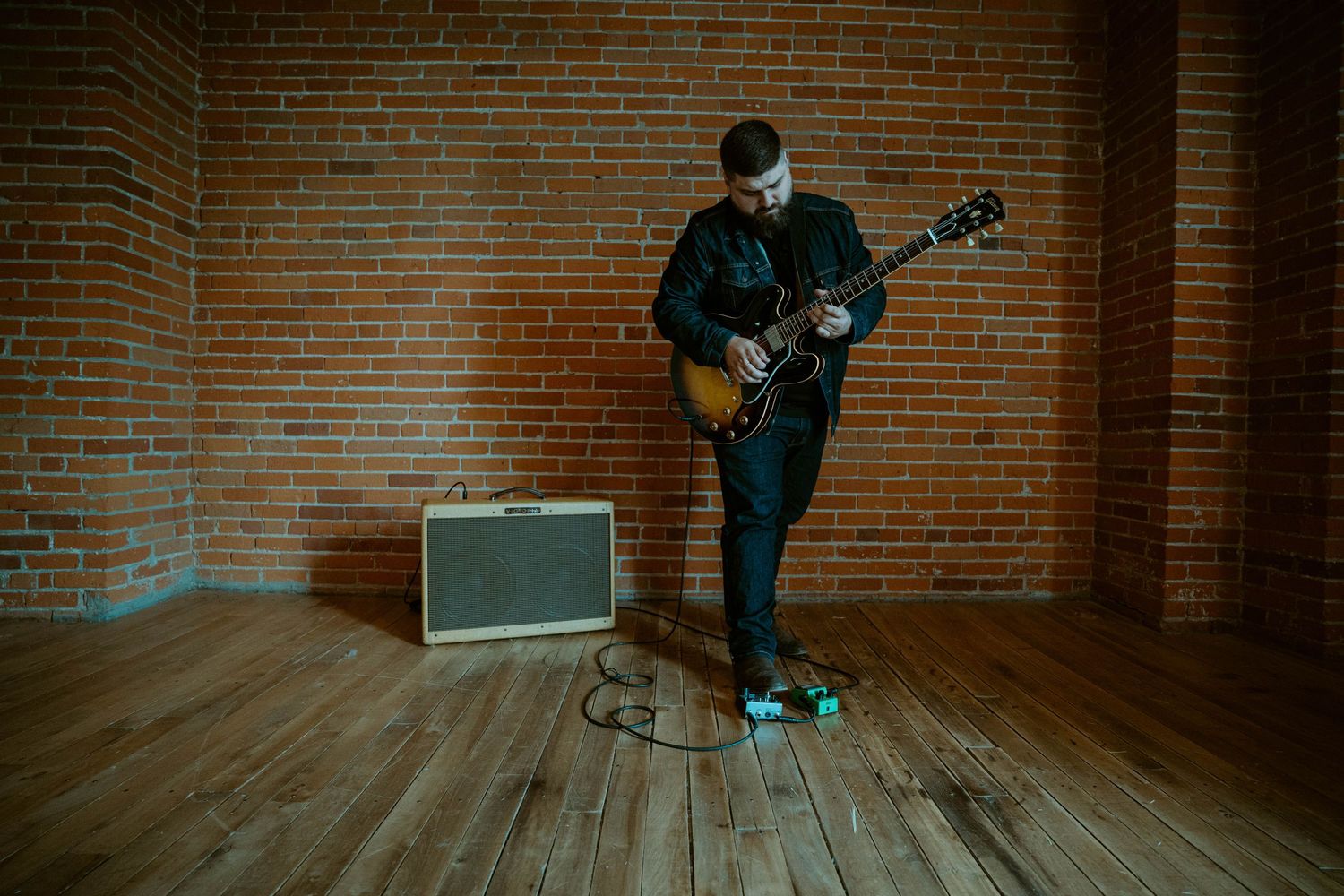 Dylan Farrell playing electric guitar next to an amplifier against a brick wall in a dark room.