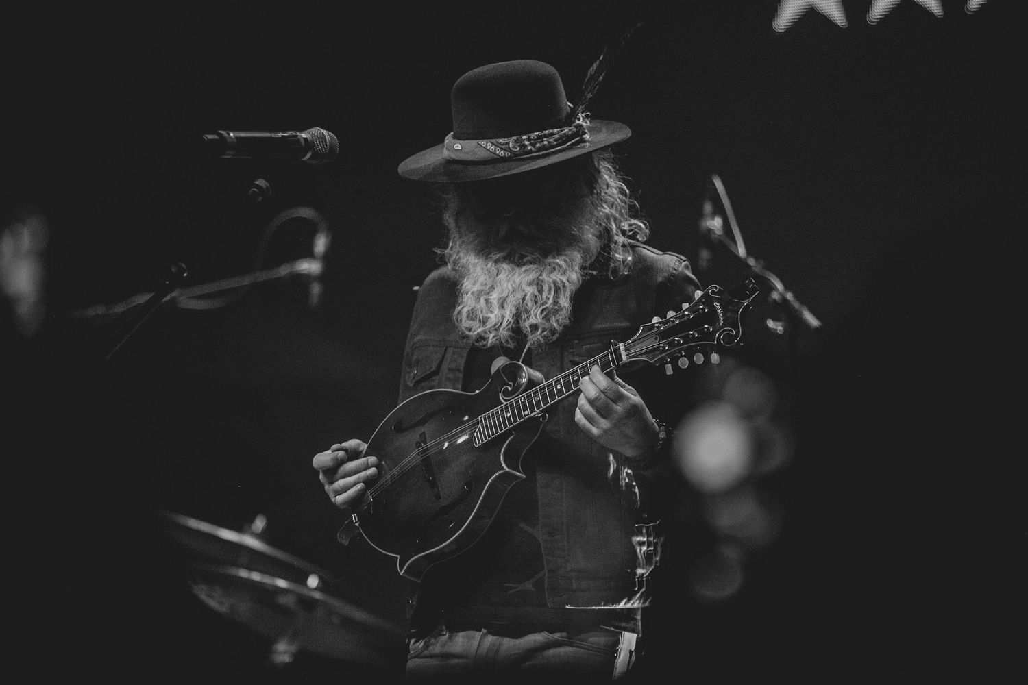 Musician in hat playing guitar against dark background at live performance.