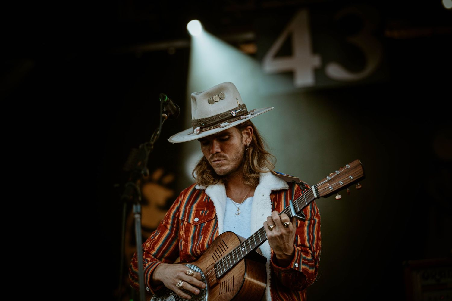Guitar player wearing cowboy hat performs on stage under spotlight.