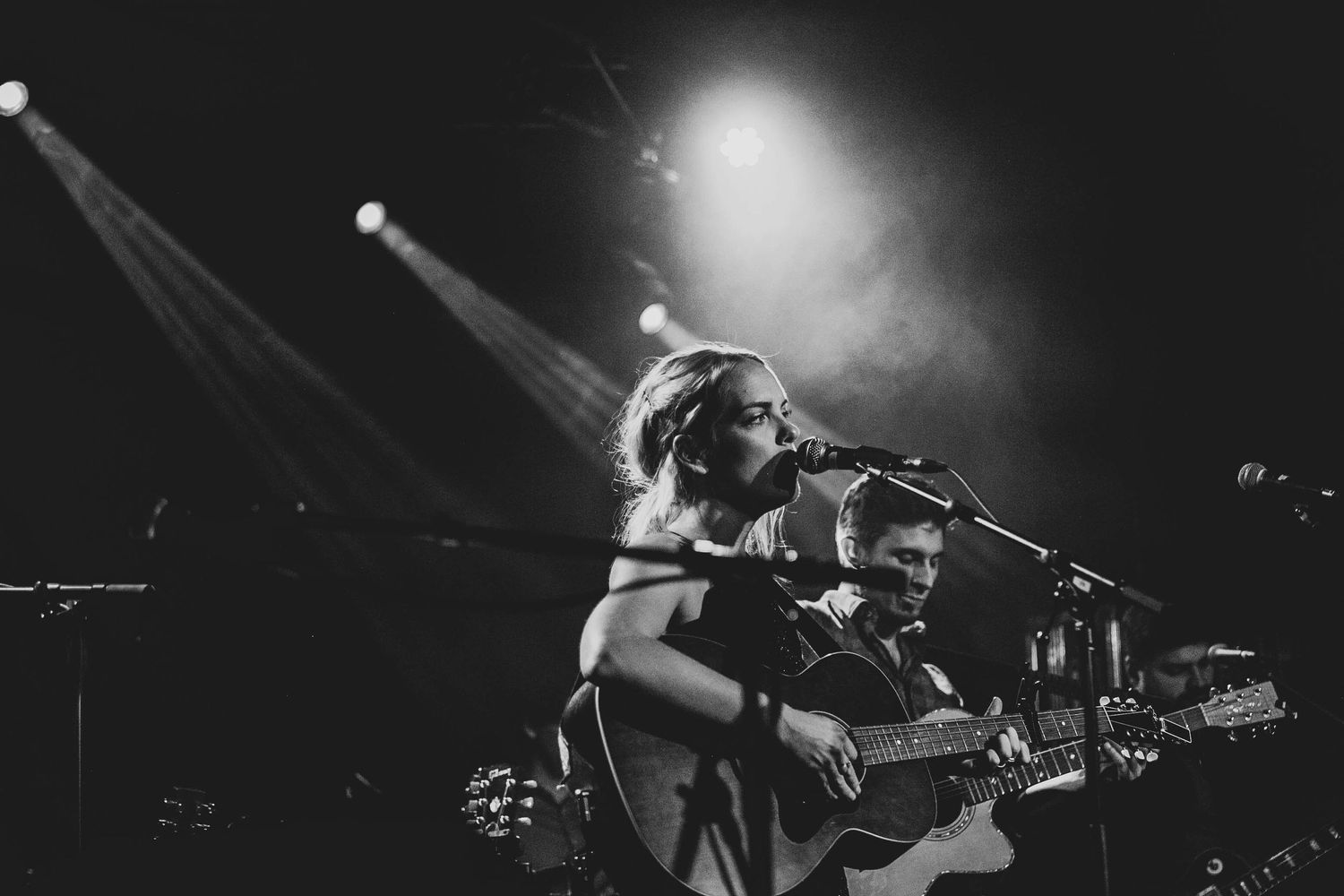Musicians performing on stage with spotlights in dramatic black and white.