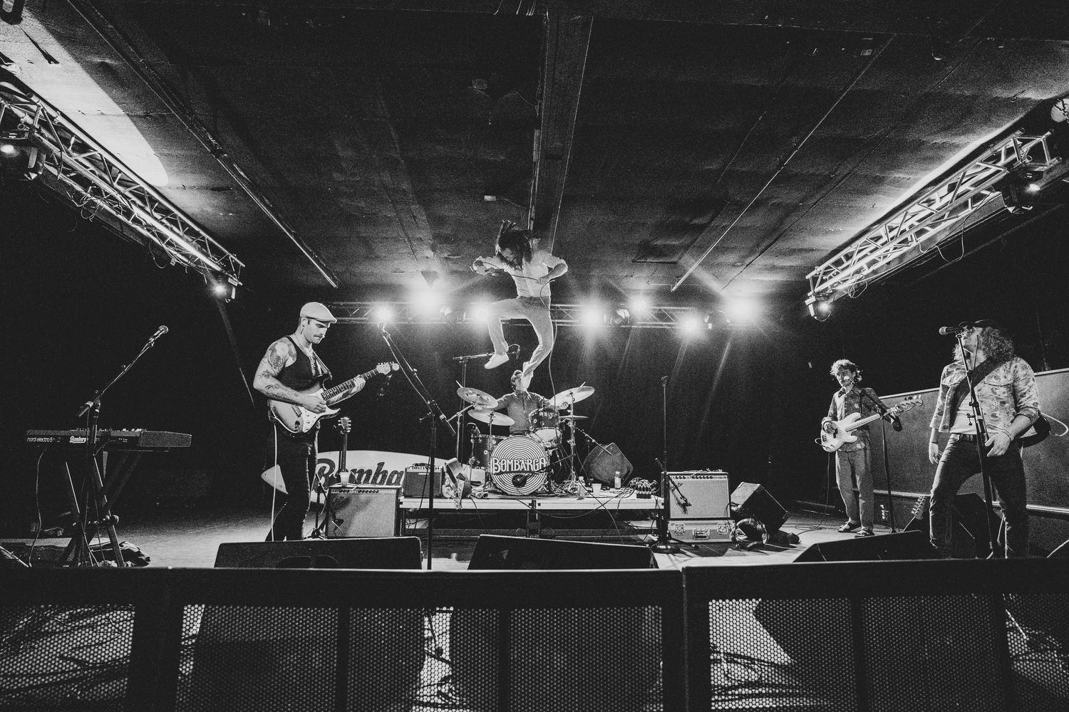 A black and white concert photo of Bombargo performing on stage under dramatic lighting.