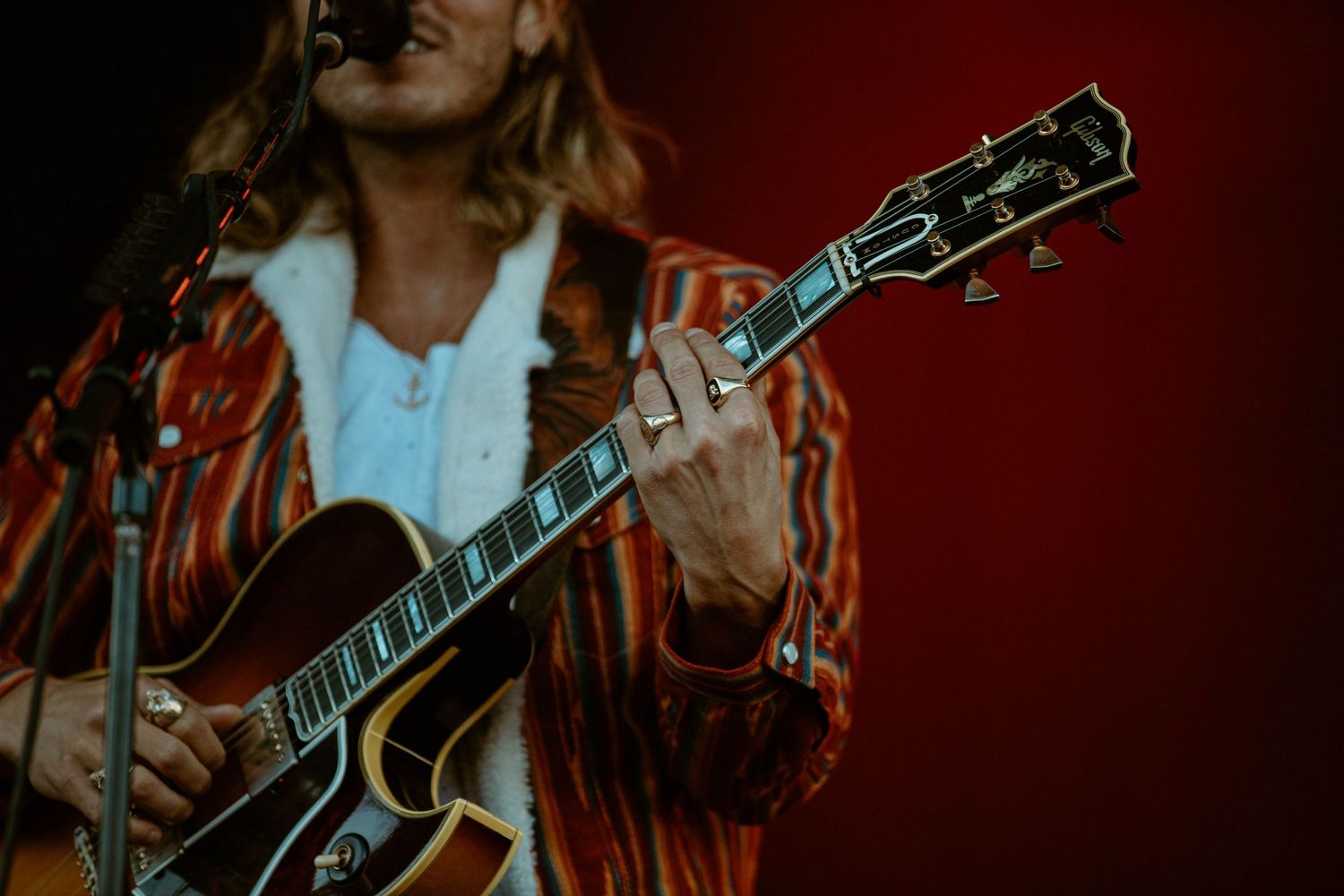 Musician playing acoustic guitar in dramatic lighting against red backdrop.