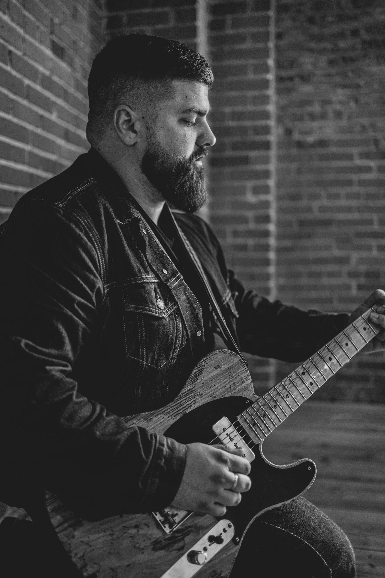 Dylan Farrell in denim plays electric guitar in a moody black and white portrait.