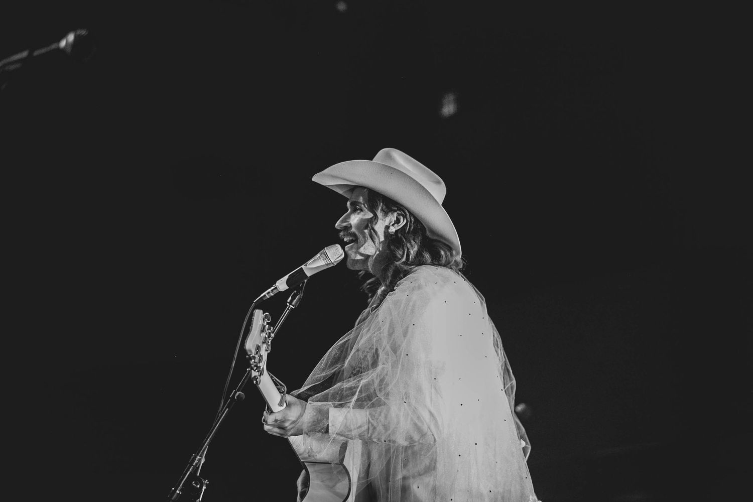 Performer in cowboy hat singing into microphone during stage performance.