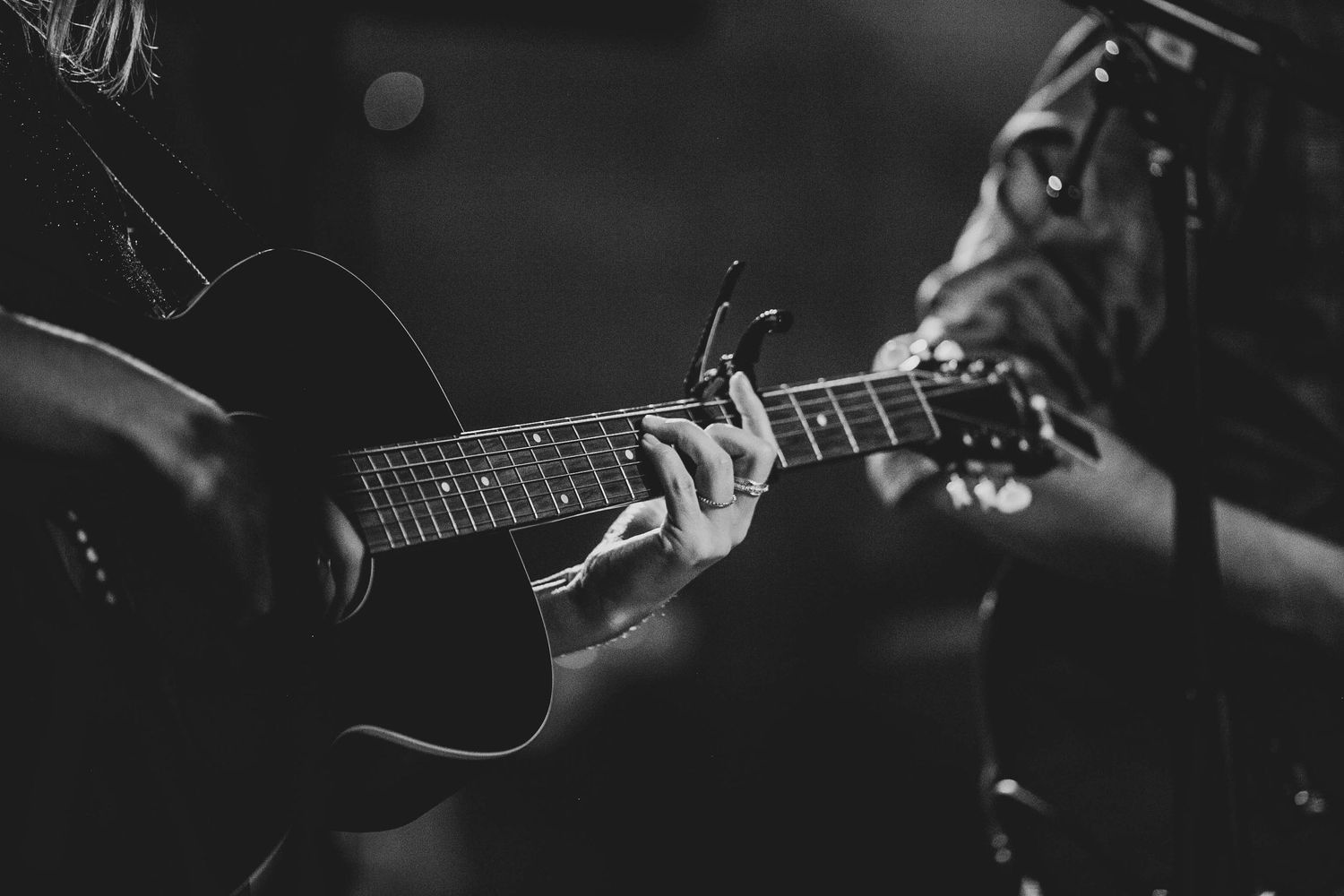 Black and white close-up of hands playing acoustic guitar strings.