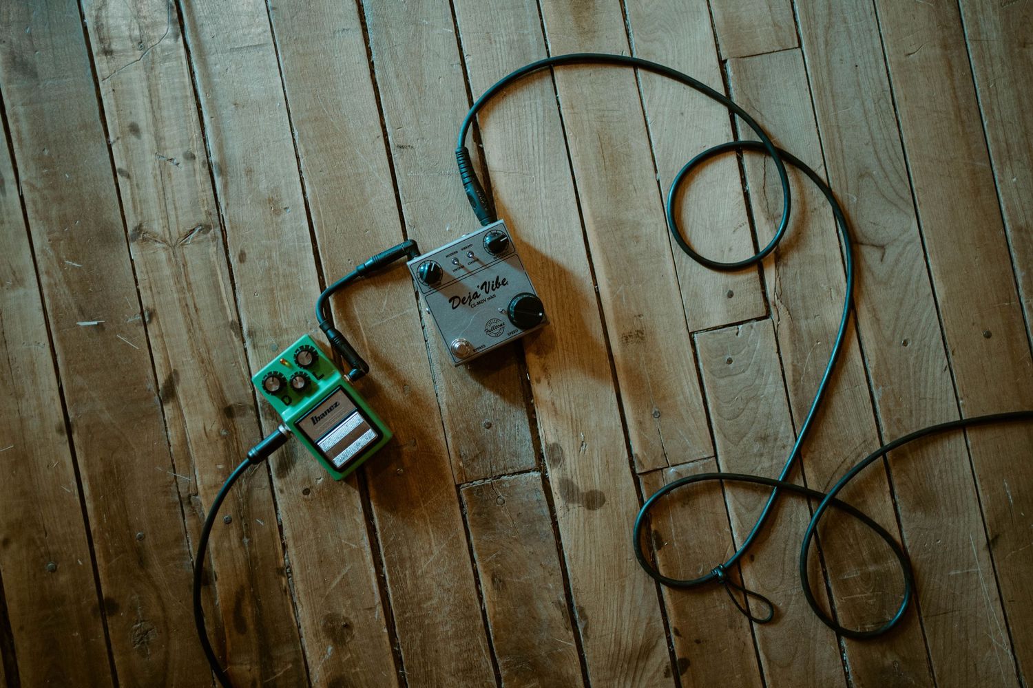 Guitar pedals and cables arranged on a wooden floor.