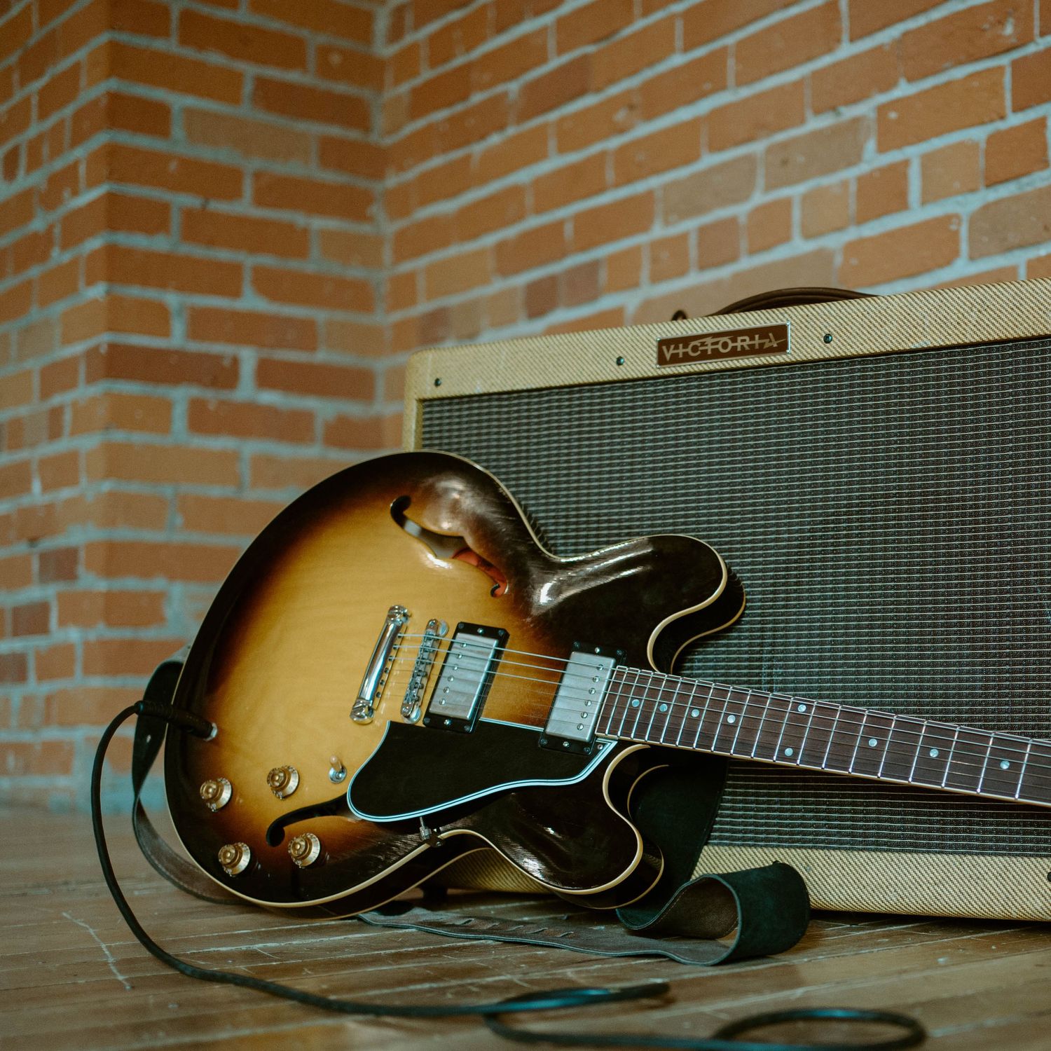 A sunburst Gibson semi-hollow electric guitar rests against a vintage amplifier on wooden floor.