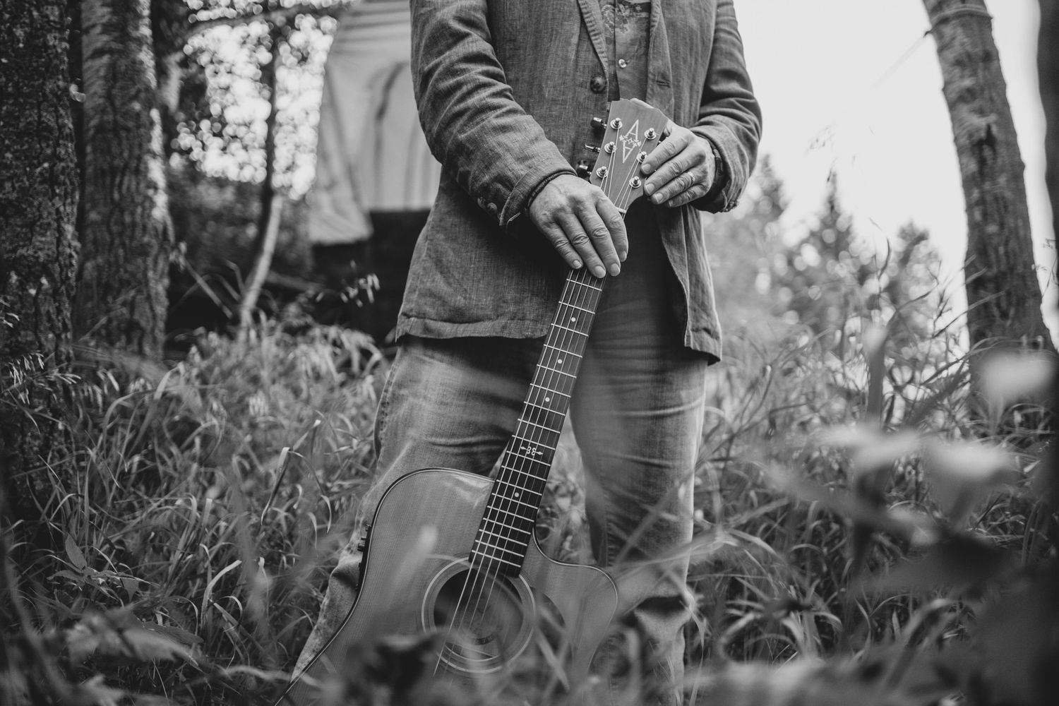 Black and white photo of Tim Isberg holding guitar outdoors among tall grass.