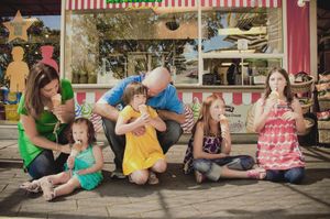 Family with four children enjoying ice cream outside a colorful shop on a sunny day.