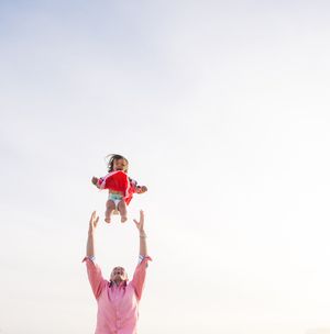 Parent tossing a laughing baby high into the air against a bright open sky.