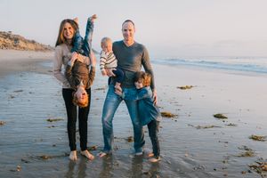 Happy family of four with two toddlers posing playfully on a scenic California beach.