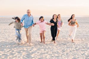 Happy family of six running together on white sand beach at sunset.