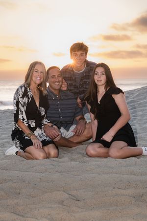Family of five smiling together on sandy beach at golden sunset.