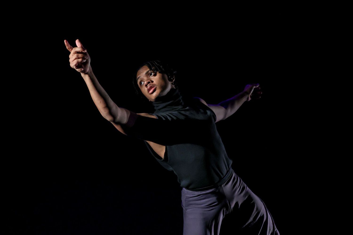 Expressive dancers perform contemporary piece against black background on theater stage.