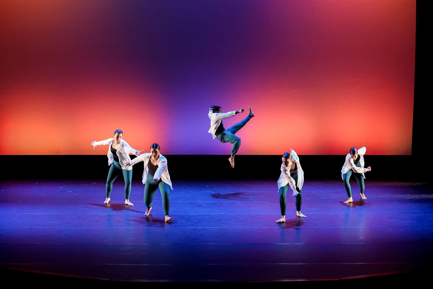 Modern dancers perform on a stage with deep blue and red lighting effects.