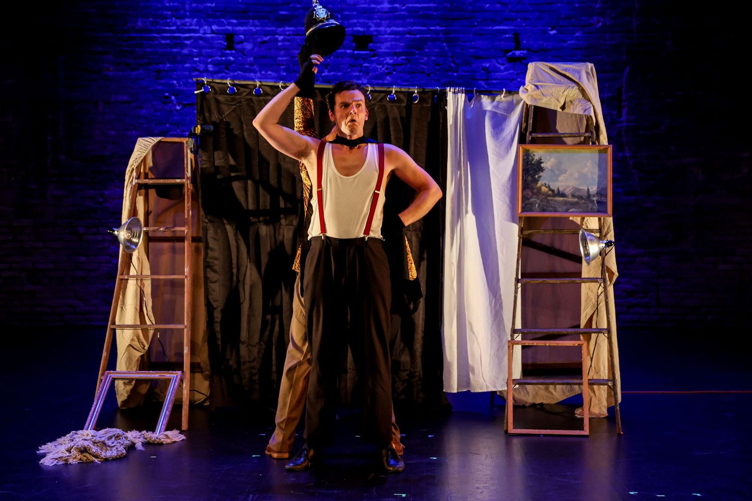 Stage performers in blue lighting create dramatic silhouettes against a dark backdrop with wooden ladder props.