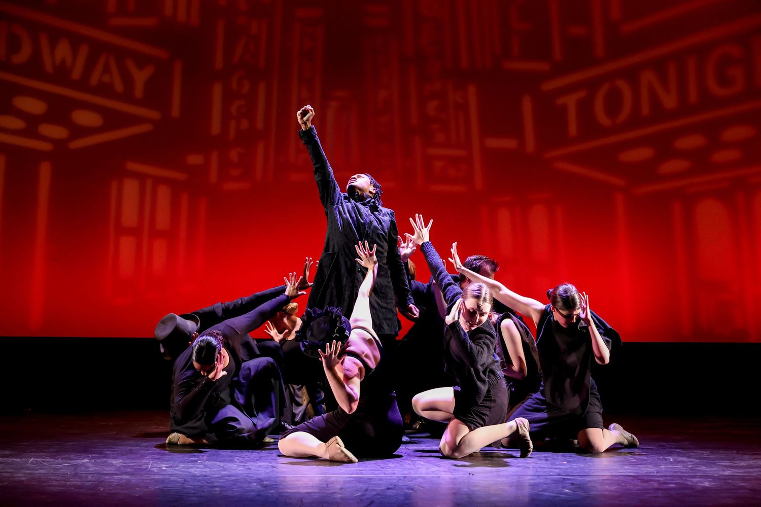 Dance performance on stage with red backdrop featuring dynamic group choreography.