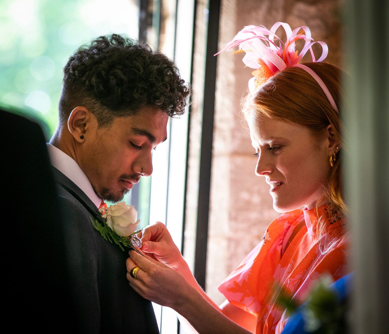 Intimate moment captured between couple in formal attire near window with warm lighting.