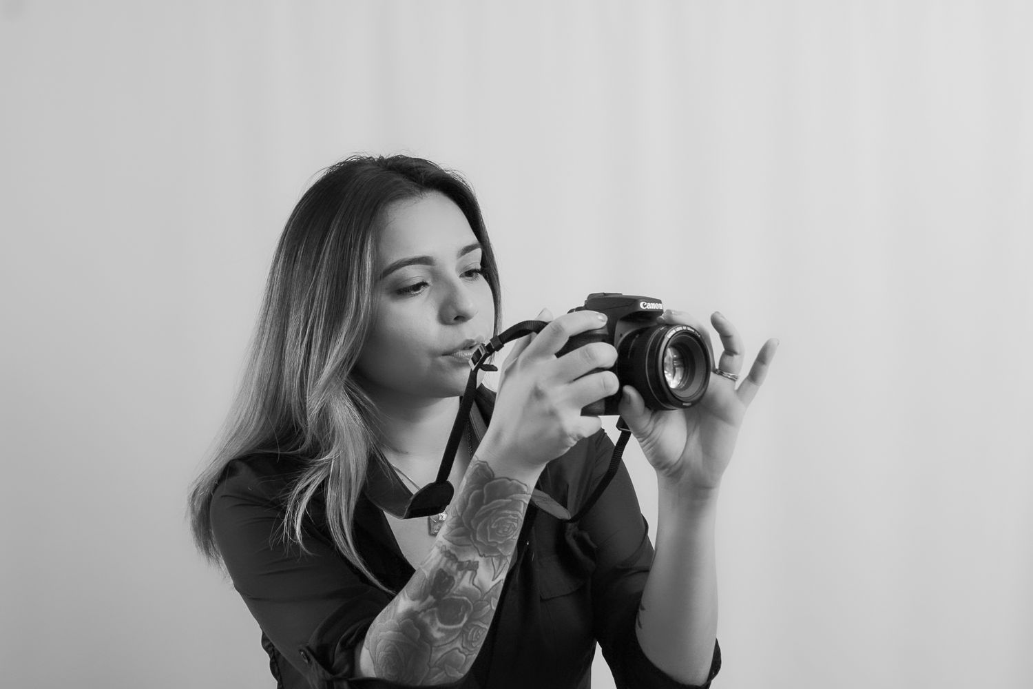 A photographer with tattoos examines a camera against a light background.