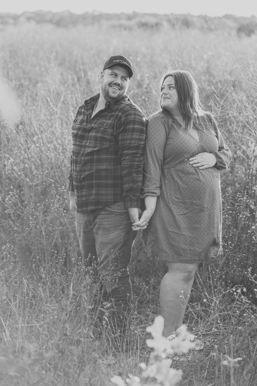 A couple poses together in a tall grass field during a black and white photo session.