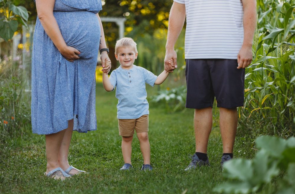 A family moment captured in a lush garden with corn stalks in the background.