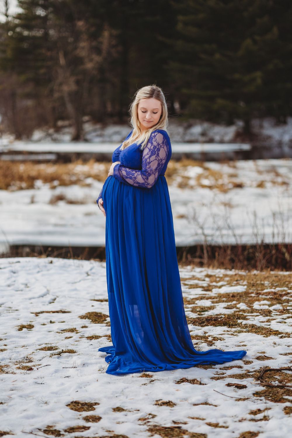A woman in a royal blue lace dress poses gracefully in a snowy field.