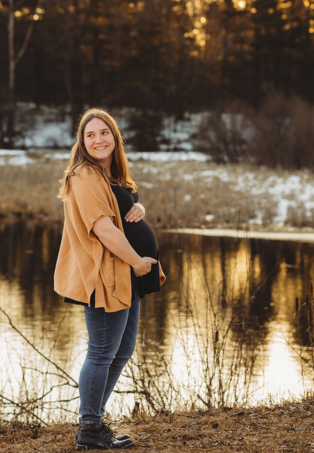 Golden hour engagement photos by lake with couple in mustard sweater and dark attire.