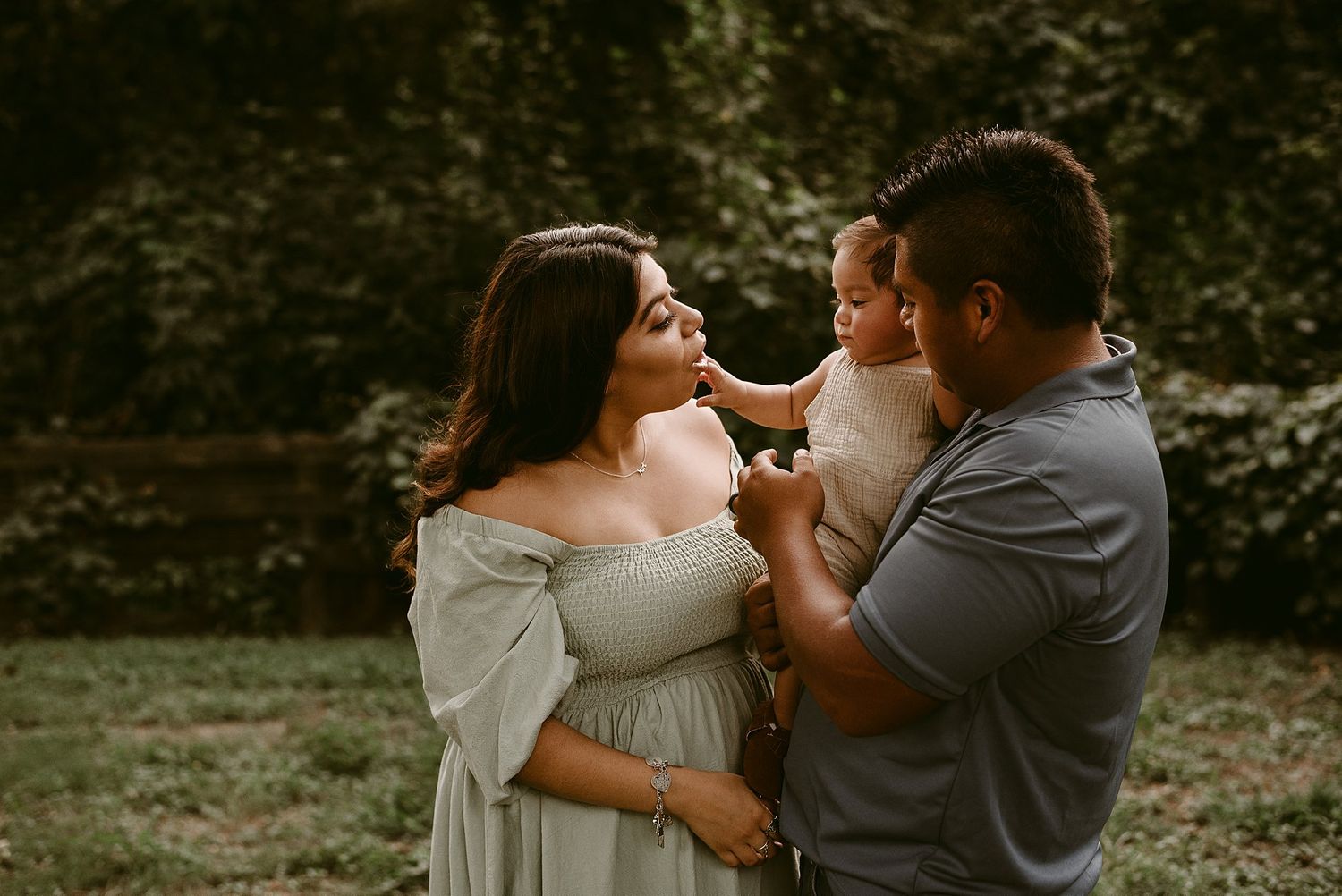 Family shares intimate moment outdoors in soft golden light wearing casual grey attire.