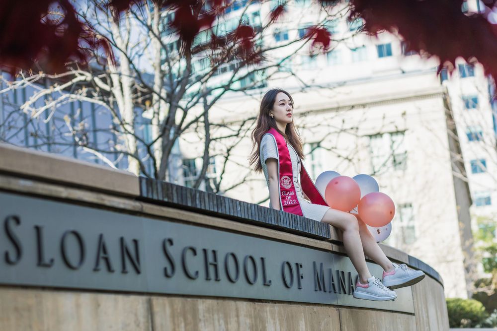 Graduate celebrating with balloons outside the MIT Sloan School building.