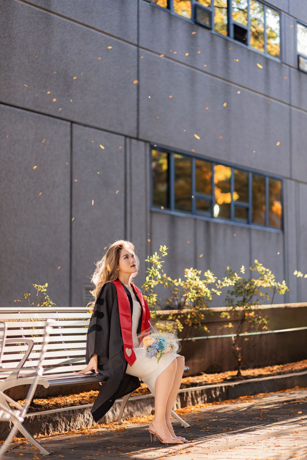 Graduate sitting on bench near modern building facade in autumn lighting.