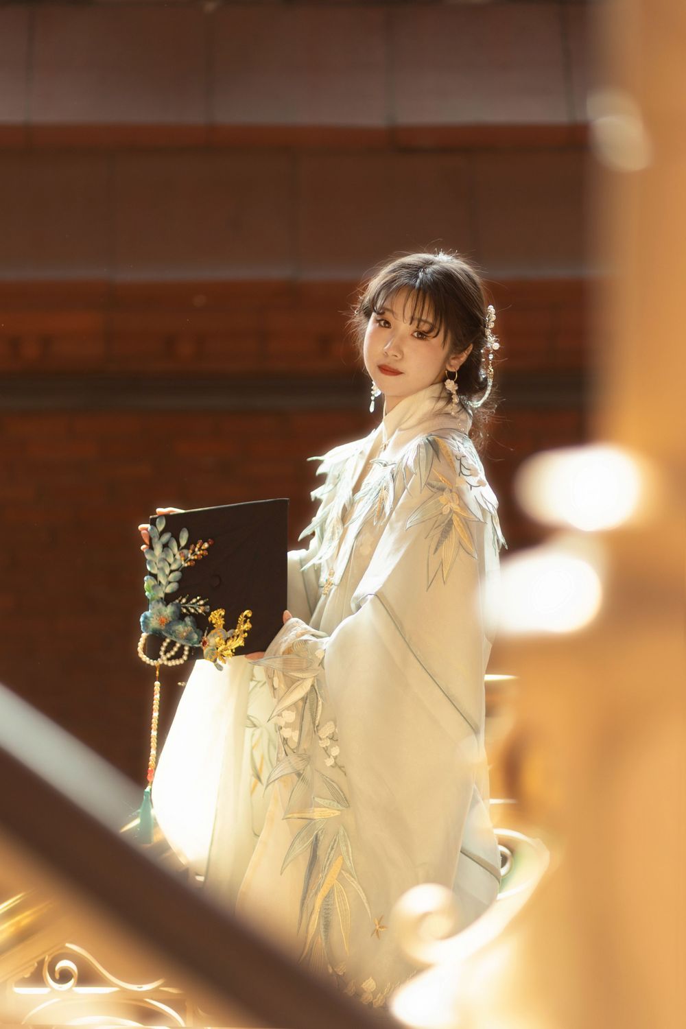 Ethereal figure in flowing white dress poses gracefully against warm lighting and decorative railing.