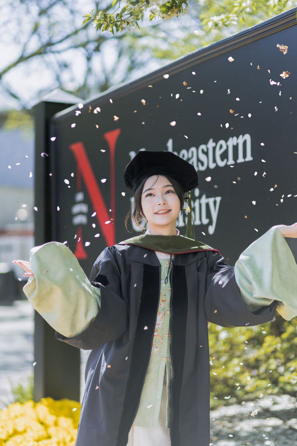 Outdoor campus scene with falling confetti against dark background and university signage.