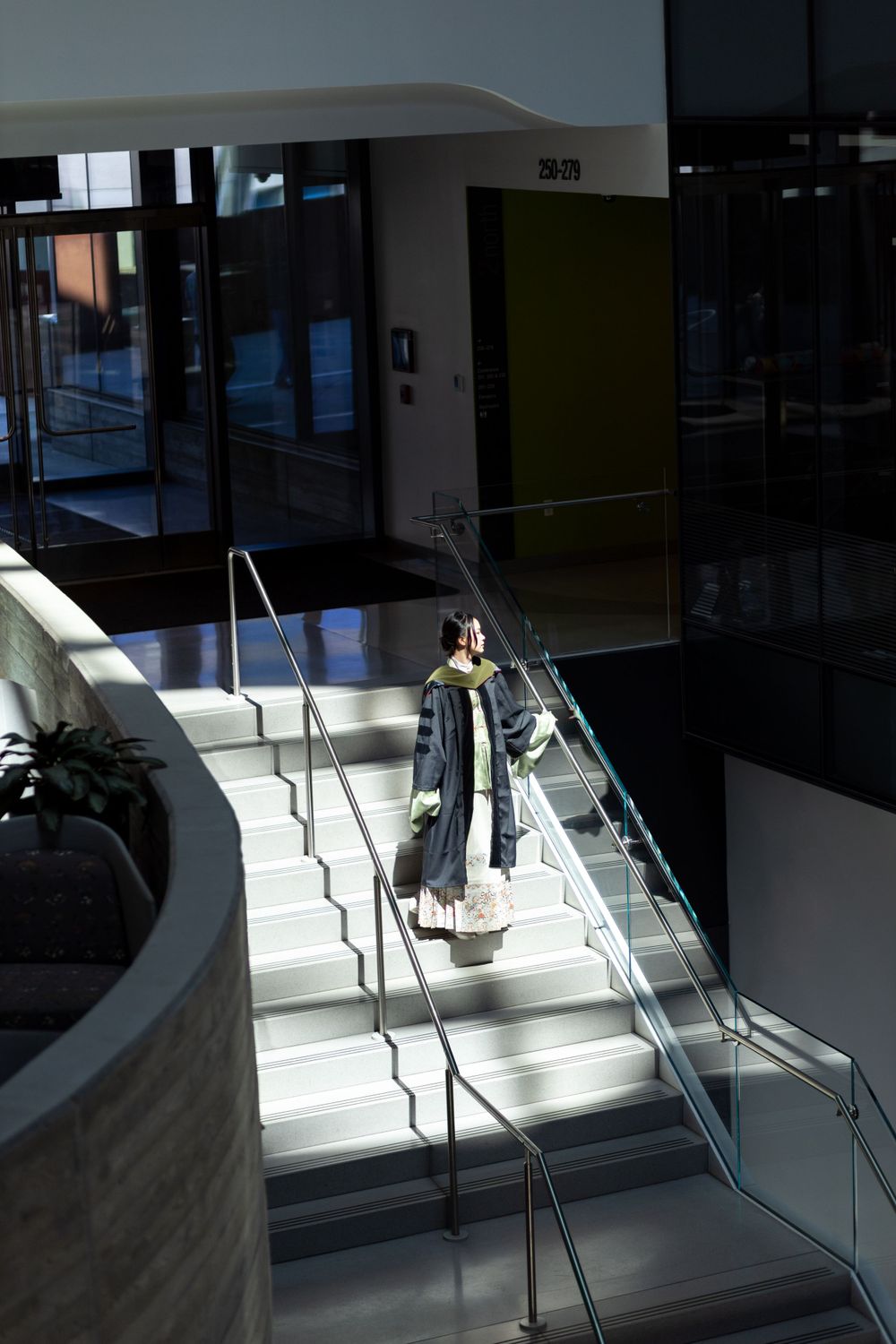 Graduate descends modern staircase in dramatic lighting at academic building.