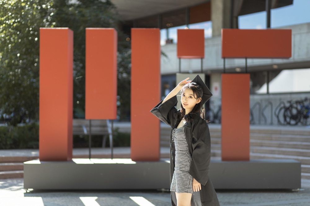 Graduate poses in front of red architectural pillars at modern campus building.