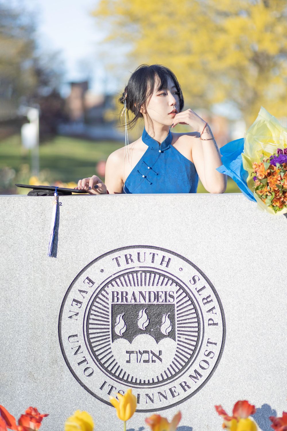Student poses with Brandeis University seal during graduation photoshoot.