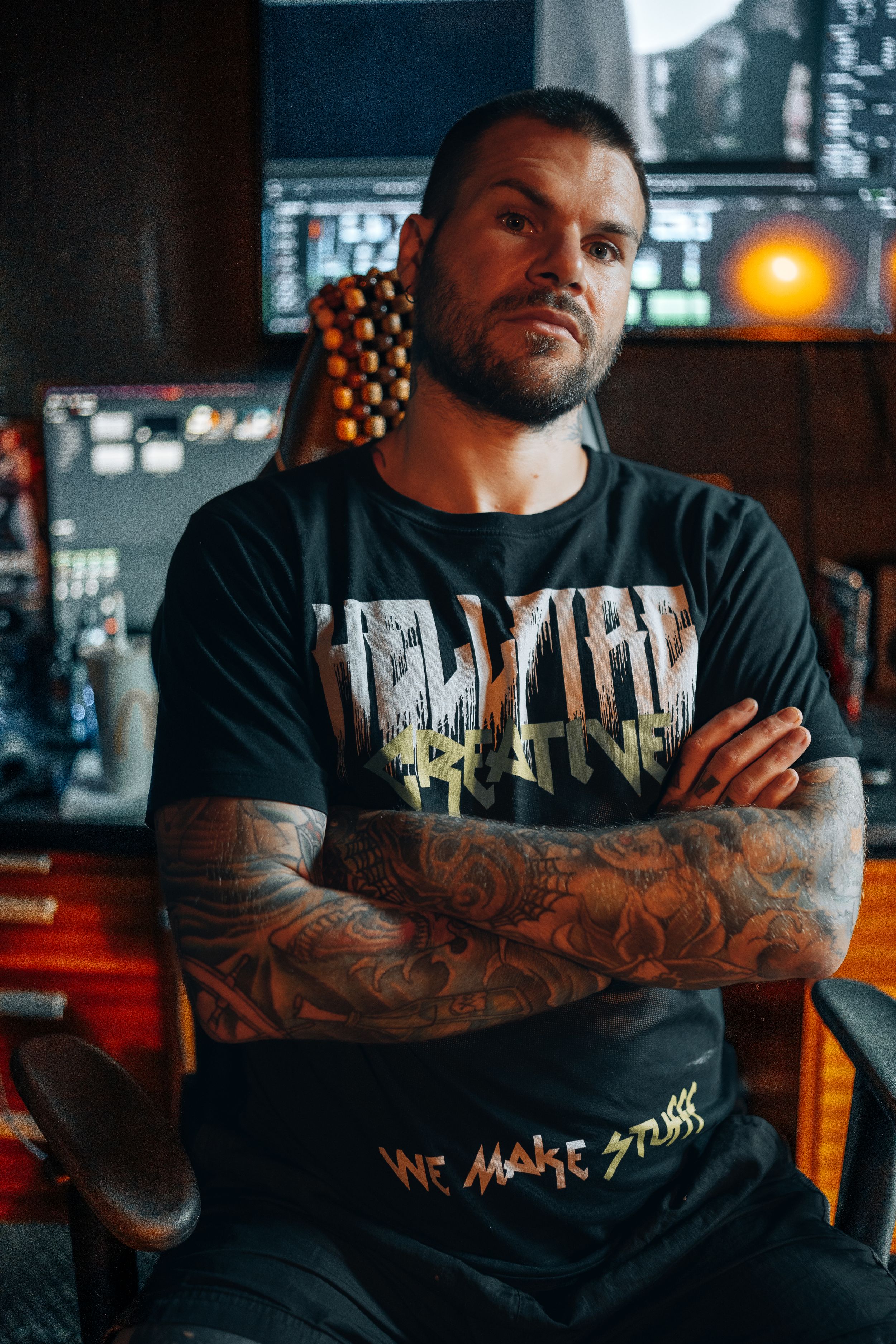 Person with tattoo sleeves wearing black graphic t-shirt poses in dimly lit urban setting.