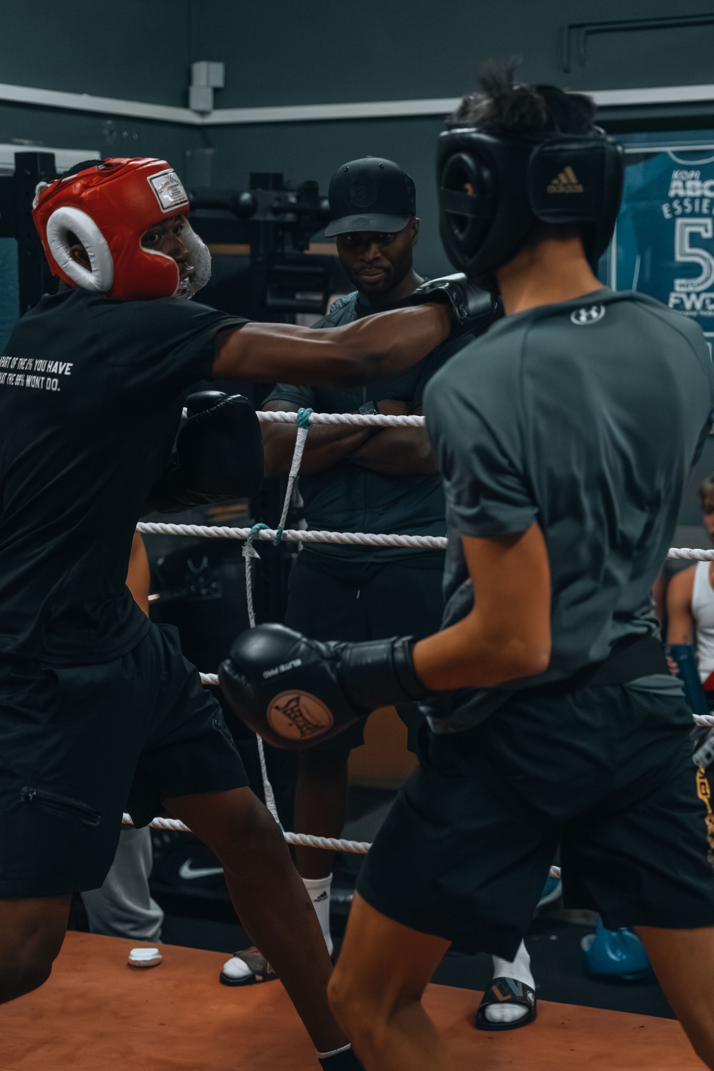 Boxers training in a dark gym with ropes and equipment visible in the background.