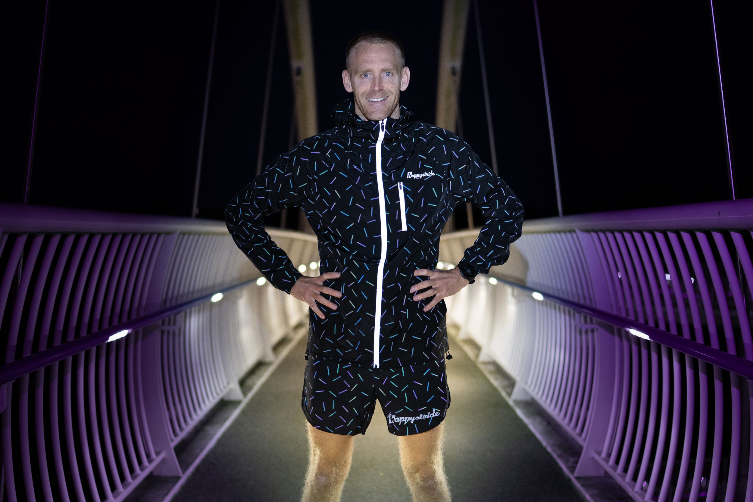 Figure walks through dramatically lit purple tunnel wearing black patterned jacket.