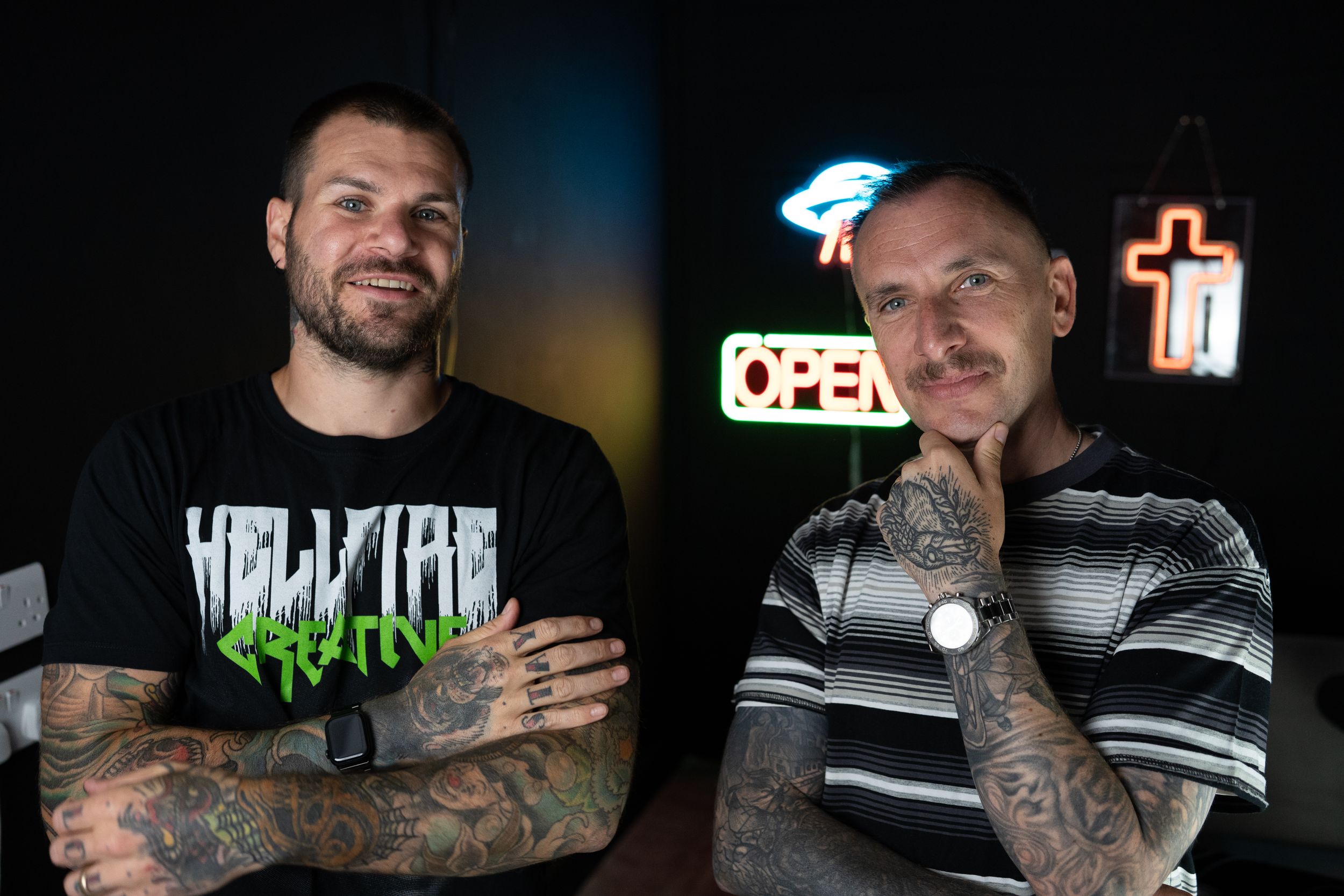 Two people smile in front of blue neon lights wearing graphic t-shirts.