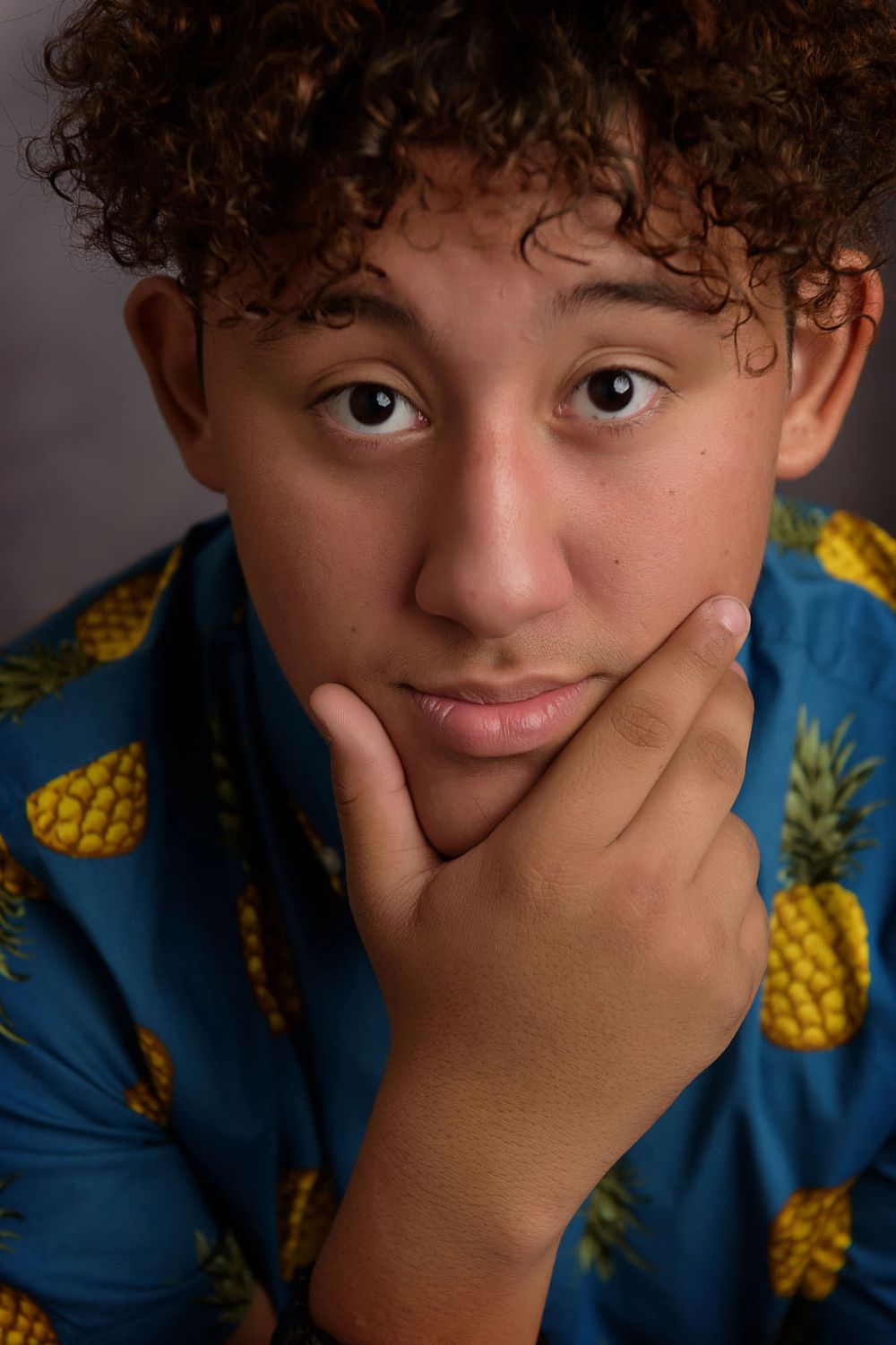 Portrait in a vibrant pineapple-print shirt with hand posed thoughtfully on chin.