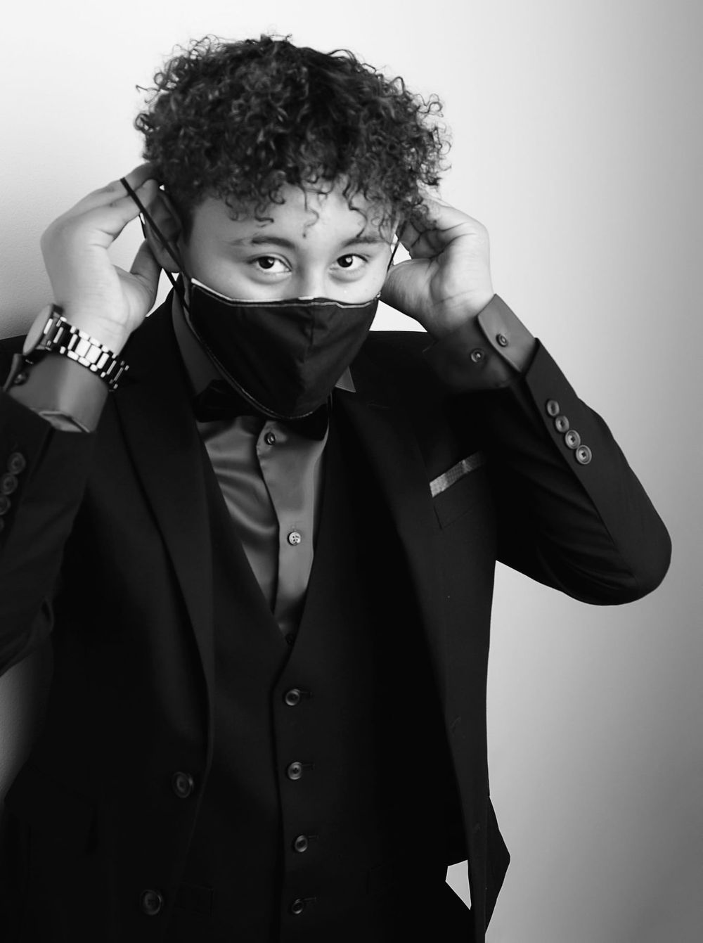 Black and white photo of someone in formal wear adjusting a face mask.