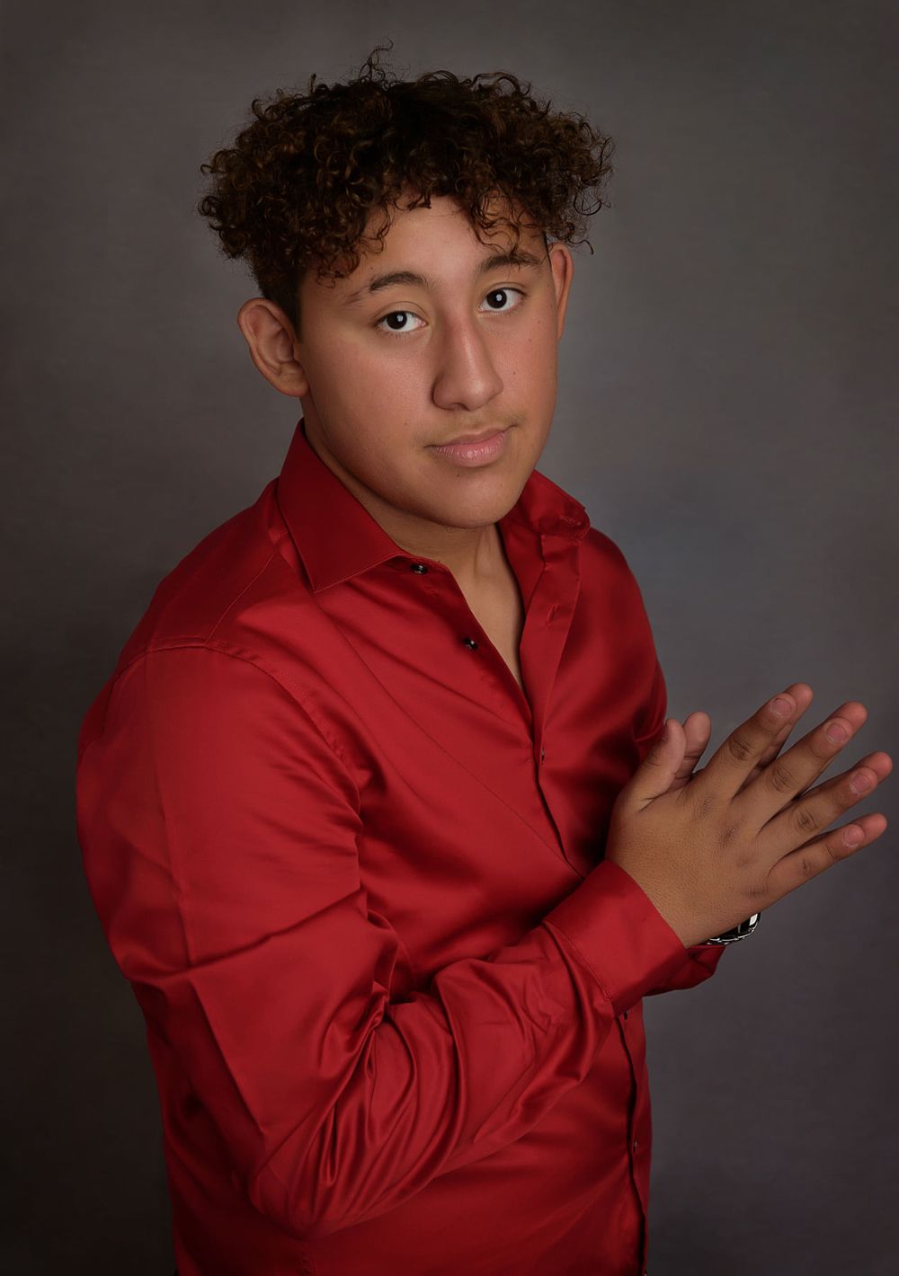 Studio portrait with subject wearing a vibrant red dress shirt while posing expressively against dark background.