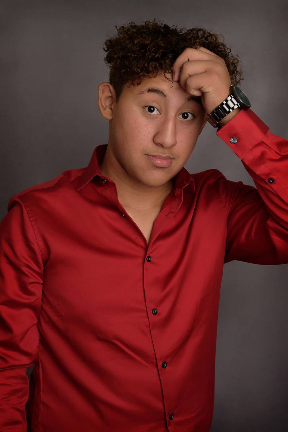 Young person in a stylish red button-up shirt poses against dark background.