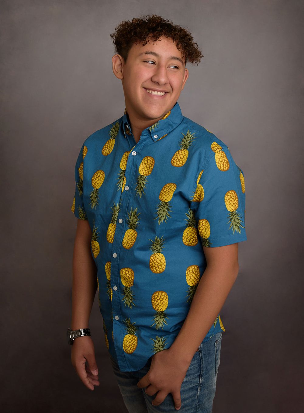 Person wearing blue shirt with pineapple print poses against grey backdrop.