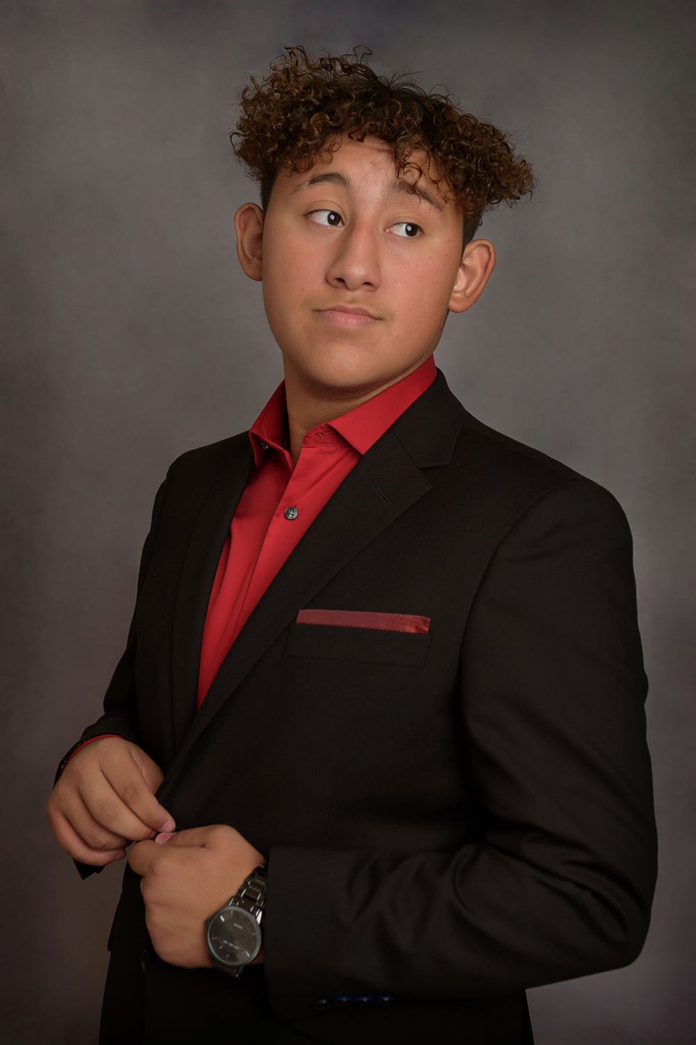 Professional portrait showing formal attire with red shirt and black blazer while wearing wristwatch.