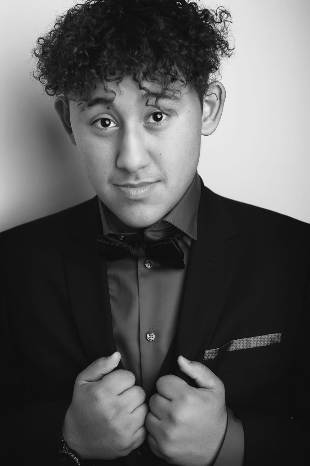 Black and white studio portrait showing formal attire with bowtie and textured pocket square.